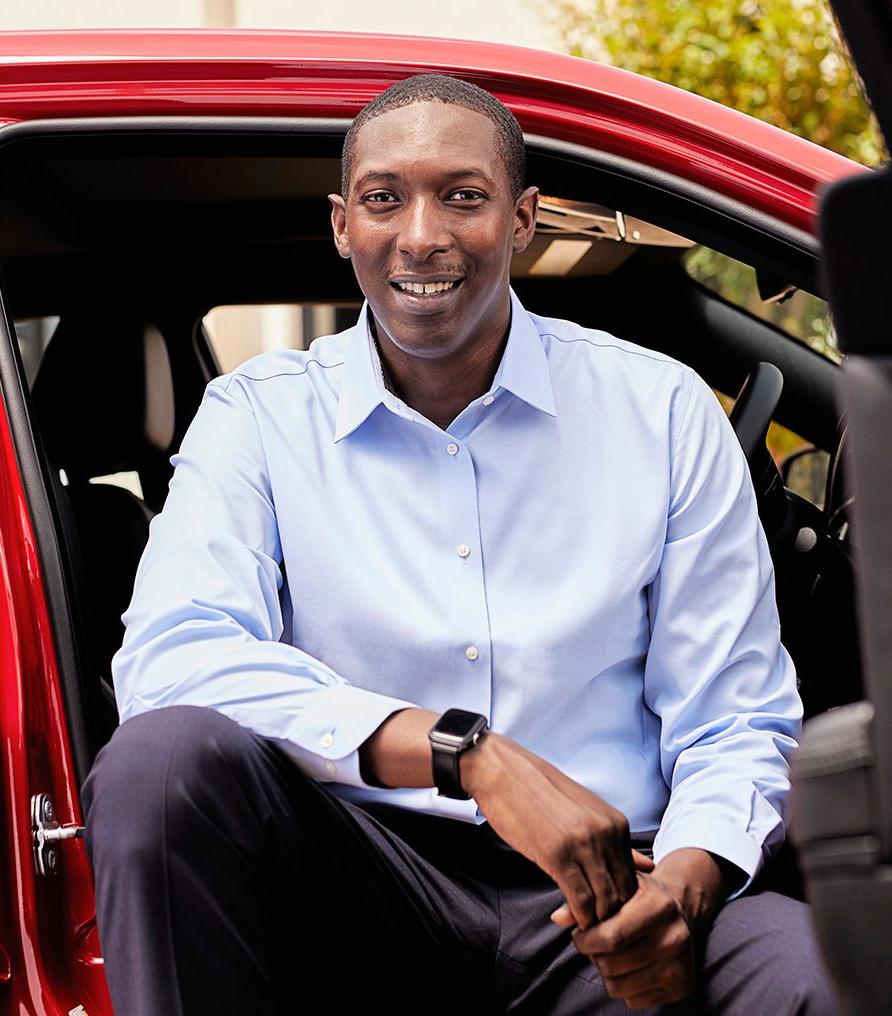 穿着浅蓝色衬衫的深色皮肤的绅士坐在一辆红色的车里，面带微笑.